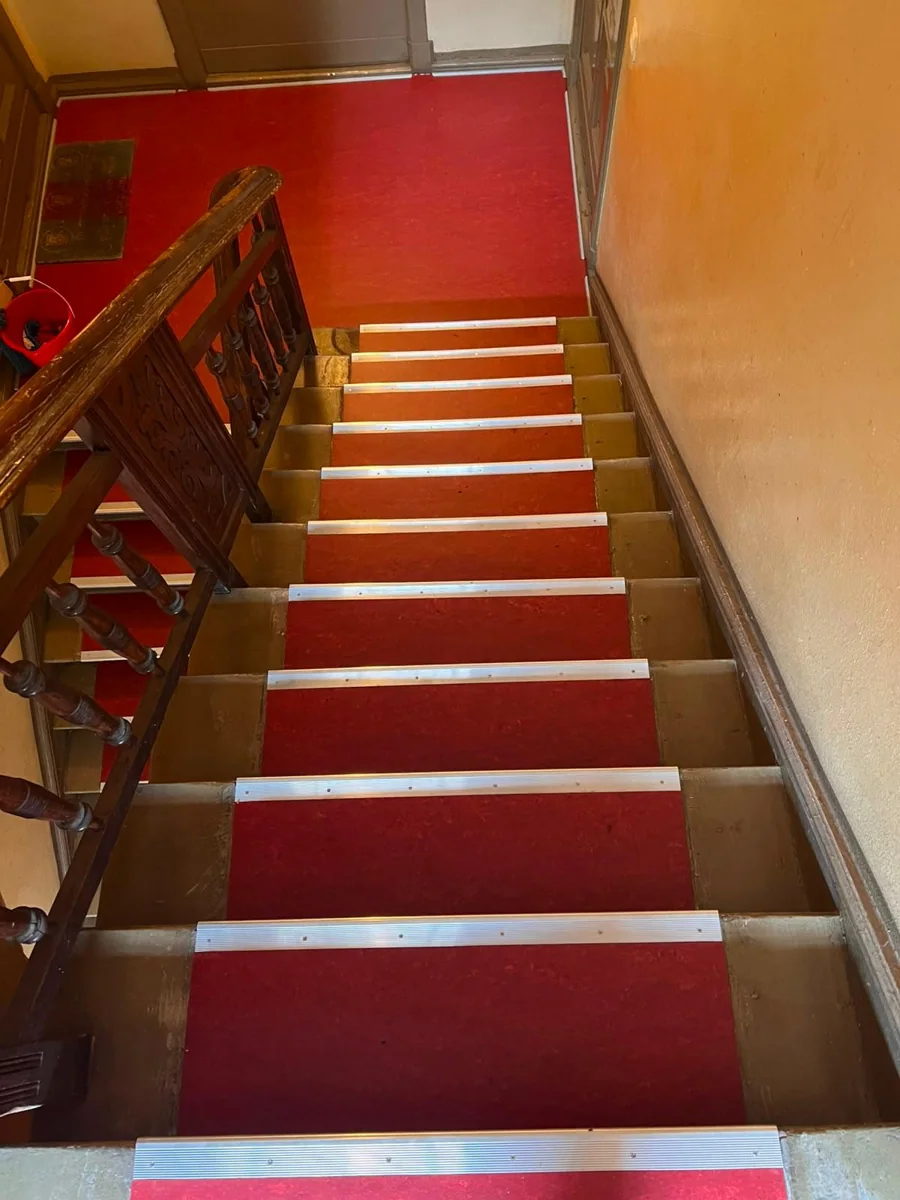 Treppe mit rotem Bodenbelag und Metallprofilen, Blick zum Eingang